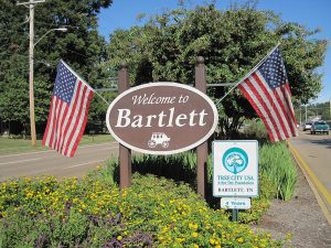 Welcome sign for Bartlett, TN, with American flags, vibrant landscaping, and Tree City USA recognition. Expert lawn care services available in Bartlett and surrounding Mid-South areas.