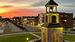 Scenic sunset view of Southaven, MS, featuring a well-lit bell tower, modern brick buildings, and a beautifully landscaped downtown area. A vibrant community with maintained green spaces and walkable streets.