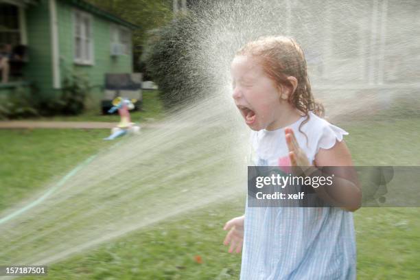 Child playing under garden hose spray on lawn maintained with weed control and fertilization in North Mississippi